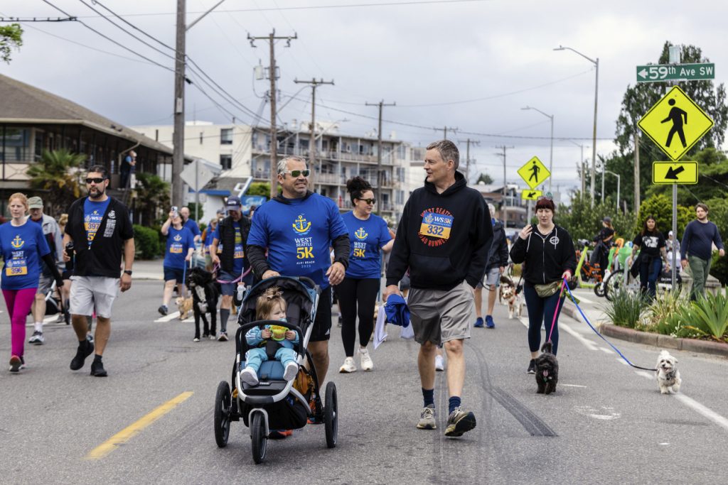 A group of people walking their dogs down a street in West Seattle during a 5K event.
