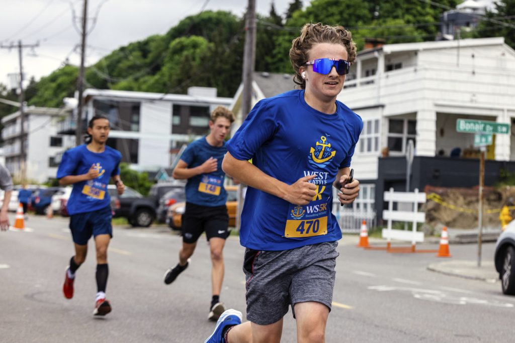A young man participating in the West Seattle 5K, running in a blue shirt and sunglasses.